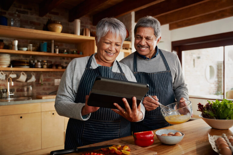 Elderly couple smiling while cooking breakfast - Harmony at Home Senior Care